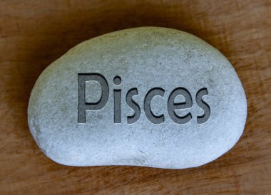 Pisces zodiac sign text engraved on a stock with wooden background. Zodiac sign concept.