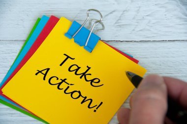Motivational and inspirational quotes text on notepad - Take Action. With hand holding pen.
