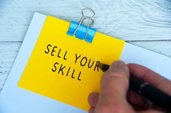 Hand writing sell your skill text on yellow notepad. Skill concept.