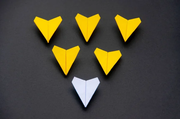 White paper plane origami leading yellow planes on dark background. Leadership skills concept.
