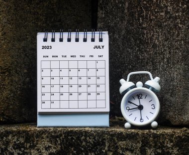 July 2023 white desk calendar with alarm clock glass on rock background. Calendar concept