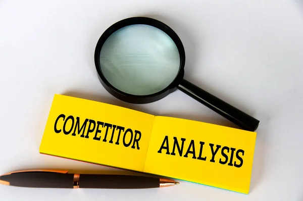 Competitor analysis text on yellow notepad with pen and magnifying glass on white background. Competitor analysis concept