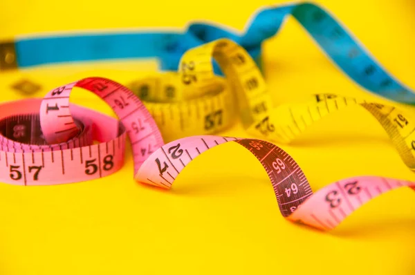 Blue, yellow and red measuring tape on yellow background. Copy space and weight loss concept