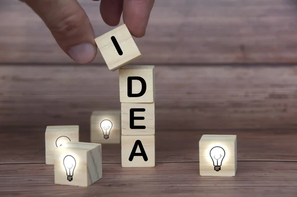 Idea text on wooden blocks surrounded by light bulbs on wooden background. Business idea concept.