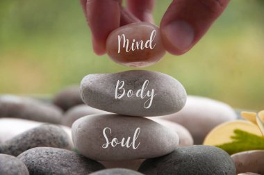 Hand holding zen stone with words Mind, Body, Soul. Spa concept. clipart