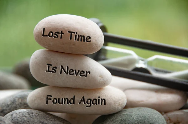 Lost time is never found again text engraved on stones with minute glass background. Copy space and time concept.