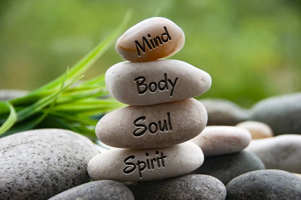 Mind, Body, Soul and Spirit words engraved on zen stones with blurred nature background. Copy space and zen concept.