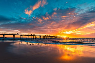 Port Noarlunga iskelesine doğru dramatik bir gün batımı izleniyor. Güney Avustralya 'da insanlar geziniyor.