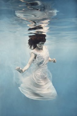    Siyah saçlı, beyaz elbiseli bir kız sanki yer çekimsiz havada yüzer gibi suyun altında yüzer.                            