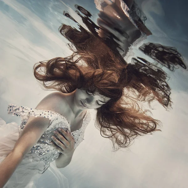 黒い髪をした白いドレスの少女がまるで飛び立つかのように水中で泳いでいる — ストック写真