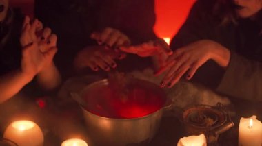 Three young girls dressed in witch's outfit are conjuring over the witch's cauldron, hands and cauldron close-up. Halloween's horror. Scary tale. Night fairy tale.