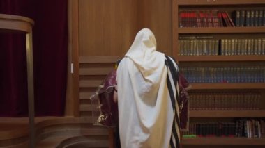 Sinagogda bir Yahudi dua ediyor. Bir adam başkanlığın yanında duruyor ve bir kitap okuyor. Dikiz Aralığı