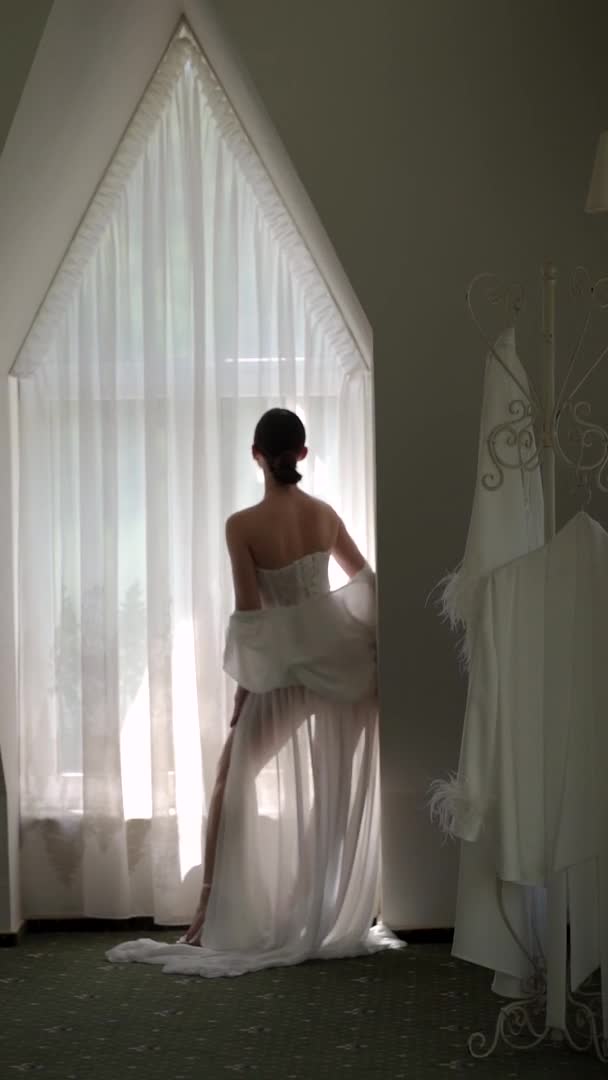 Κάθετα Βίντεο Όμορφη Νύφη Ένα Λευκό Μπουρνούζι Στέκεται Στο Παράθυρο — Αρχείο Βίντεο