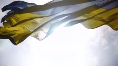 Rüzgar mavi gökyüzünün arka planına karşı Ukrayna bayrağını sallıyor. Güneş ışınları yüksek detaylı dokuyla kumaştan parlar. Ulusal mavi sarı renkli Ukrayna bayrağı. Yakın plan.