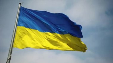The camera quickly pans from the sky to the flag. The flag of Ukraine in blue and yellow colors flutters in the air against the background of the blue sky.