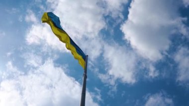 The camera moves around the flag of Ukraine. The blue and yellow flag is blowing in the wind. A flag made of high-quality textiles flutters in the air against the background of a beautiful blue sky.