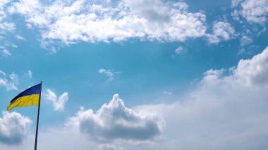 Pan camera movement with a stop near the flag. The blue-yellow flag of Ukraine flutters in the wind. A flag made of high-quality textiles flutters in the air against the background of a beautiful sky.