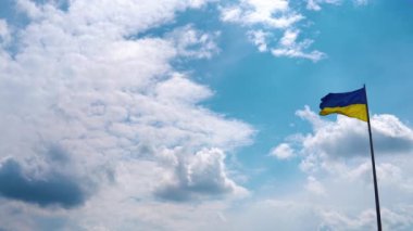 Pan camera movement with a stop near the flag. The flag of Ukraine with the national blue-yellow colors flutters against the background of the blue sky with beautiful clouds. Space for yours text.