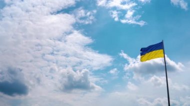 The flag of Ukraine with the national blue-yellow colors flutters against the background of the blue sky with beautiful clouds. Space for yours text.