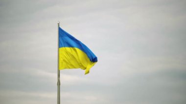 Ukrayna 'nın mavi-sarı bayrağı bulutlu, gri gökyüzünün arka planında dalgalanıyor. Metnin için boşluk.