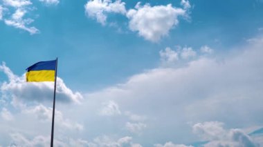 Pan camera movement with a stop near the flag. The flag of Ukraine with the national blue-yellow color is flying against the background of the blue sky with beautiful fleeting clouds. Place for text.