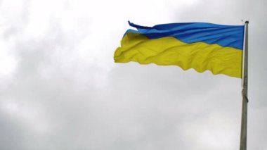 Ukrayna 'nın mavi-sarı bayrağı gökyüzünün arka planında dalgalanır. Gökyüzü kalın bulutlarla kaplıdır..
