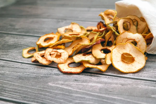 Kurutulmuş elmalar ahşap bir masanın üzerindeki beyaz bir torbadan halkalara dökülür..