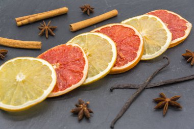 Kurutulmuş narenciye dilimleri ve siyah tahtada çeşitli aromatik baharatlar. 
