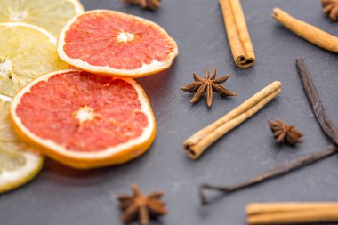 Kurutulmuş narenciye dilimleri ve siyah tahtada çeşitli aromatik baharatlar. 