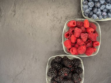 bowls with assorted berries on black slate