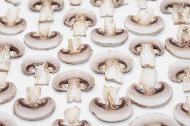 Dilimlenmiş şampiyon mantarları beyaz arka planda bir desen olarak sıralanmış.