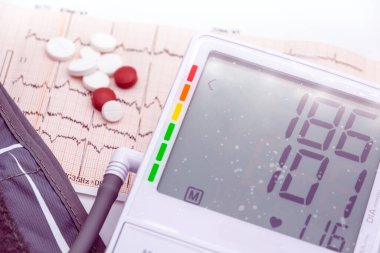 digital sphygmomanometer and heart drugs over electrocardiogram and us dollars near conceptual photo