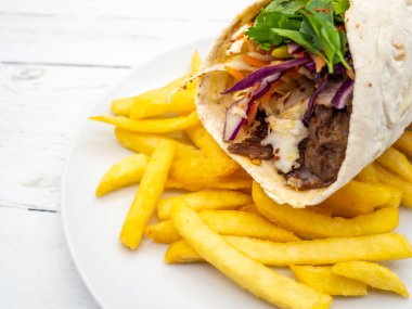 Patates kızartması ve beyaz tabakta servis edilen bir shawarma.