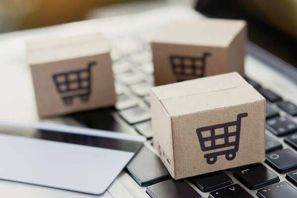 Покупки онлайн. Кредитная карта и картонная коробка с логотипом корзины покупок на клавиатуре ноутбука. Сервис покупок в Интернете. доставка на дом