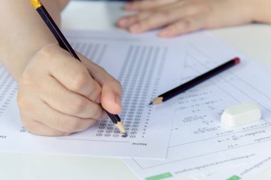 Öğrenciler, cevap kağıtları ve matematik soru kağıtları üzerinde seçilmiş kalemle yazı yazma seçeneğini el ele tutuyorlar. Sınav yapan öğrenciler. okul sınavı
