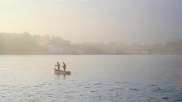 Длинный выстрел: пара рыбаков на лодке на озере Комо на закате. SLOMO — стоковое видео