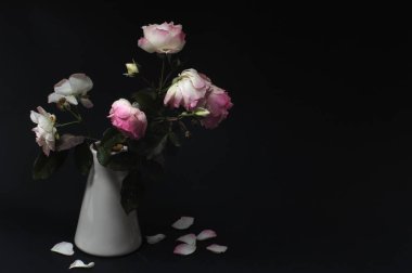 Pembe gül ve siyah arka planda yaprakları olan bir vazo. Boşluğu Kopyala