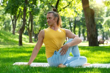 Genç adam parkta yoga yapıyor. Şehir parkında asanas yogası, güneşli bir gün. Meditasyon, refah ve sağlıklı yaşam tarzı kavramı