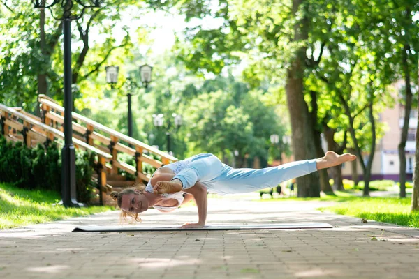 Young man practice yoga in the park. Yoga asanas in city park, sunny day. Concept of meditation, wellbeing and healthy lifestyle