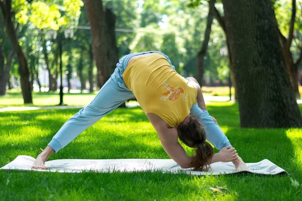 Young man practice yoga in the park. Yoga asanas in city park, sunny day. Concept of meditation, wellbeing and healthy lifestyle