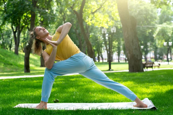 Young man practice yoga in the park. Yoga asanas in city park, sunny day. Concept of meditation, wellbeing and healthy lifestyle