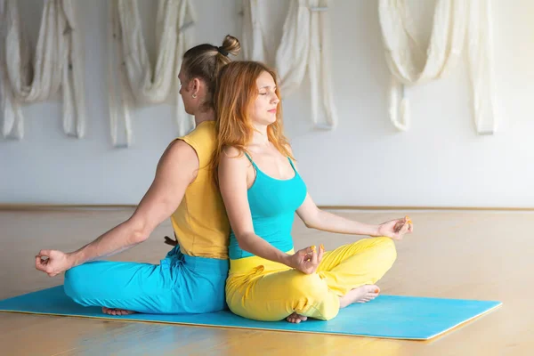 Pair yoga group  in white studio. Young couple meditating together, sitting back to back. Yoga flexibility class workout