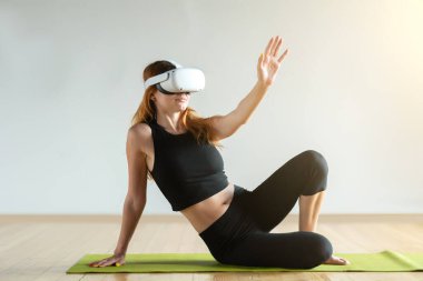 A young woman in virtual reality glasses makes fitness exercises. Future technology concept.