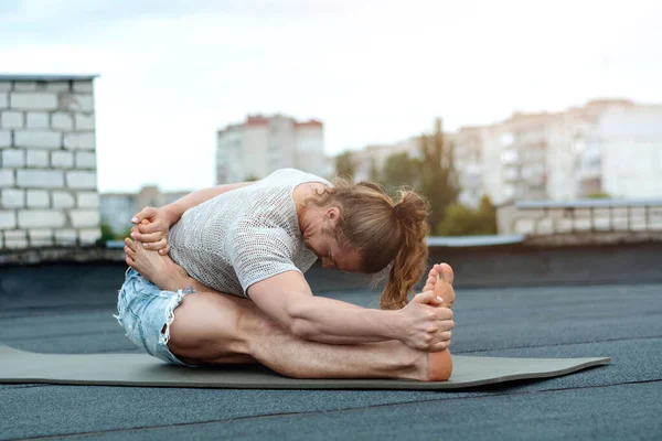 A man practices yoga on the roof of the house. Yoga at sunset. Healthy life, sport and meditation concept.