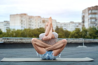 Adamın biri evin çatısında yoga yapıyor. Gün batımında yoga. Sağlıklı yaşam, spor ve meditasyon konsepti.