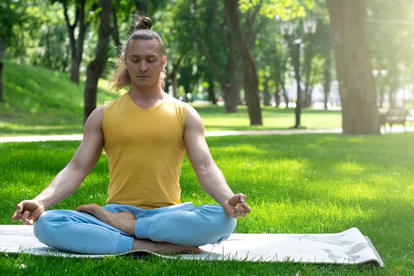 Young man practice yoga in the park. Yoga asanas in city park, sunny day. Concept of meditation, wellbeing and healthy lifestyle