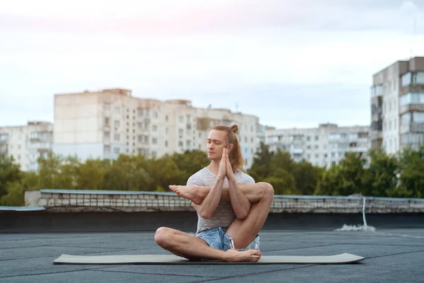 A man practices yoga on the roof of the house. Yoga at sunset. Healthy life, sport and meditation concept.