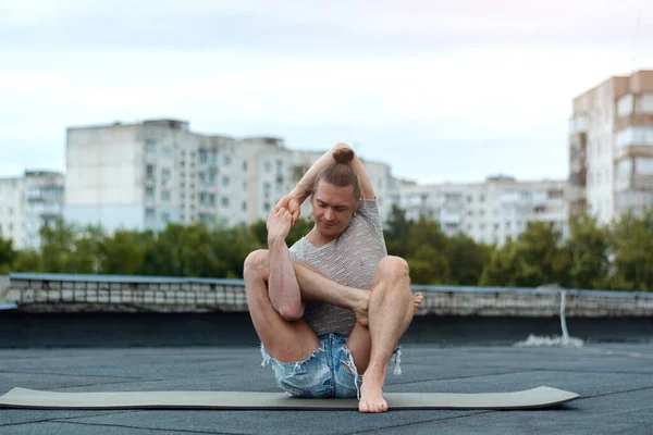 A man practices yoga on the roof of the house. Yoga at sunset. Healthy life, sport and meditation concept.