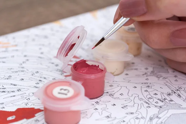 Painting by numbers. Brushes and paints on canvas close-up. A young girl is painting.