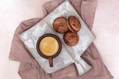A cup of coffee and chocolate macarons on a wooden board. View from above. Breakfast concept.